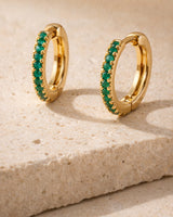 Gold-tone mini huggie hoops with green stones on textured warm stone