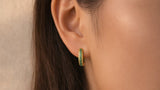 Gold-tone mini huggie hoop with green stones worn on an ear, film poster