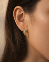 Gold-tone mini huggie hoops with green stones worn on an ear