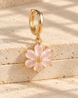 Gold-tone mini hoop with a pale-pink six-petal flower drop on textured warm stone