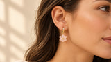 Gold-tone mini hoop with a pale-pink six-petal flower drop worn on an ear, film still