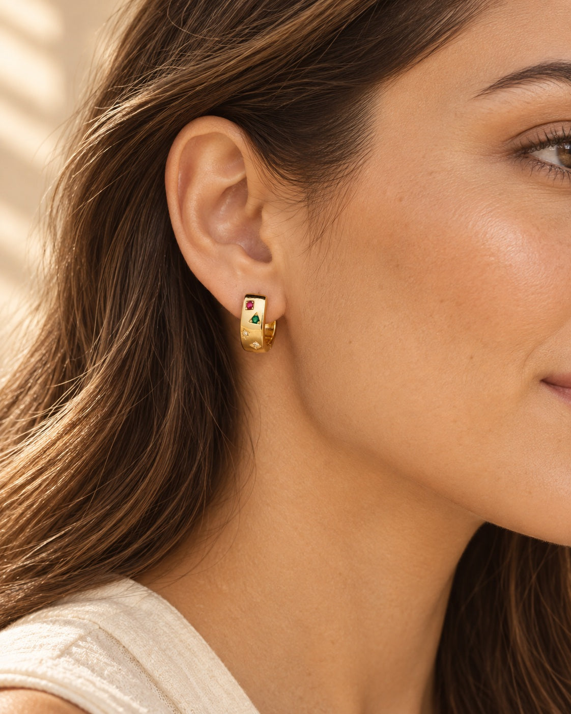 Gold-tone mini huggie hoop with multicolor square zircon stones worn on an ear