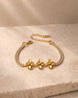 Three-flower gold-tone bracelet with double crystal-look chain on a travertine surface