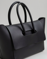 Close-up of the black structured flap tote's front flap and tubular handles