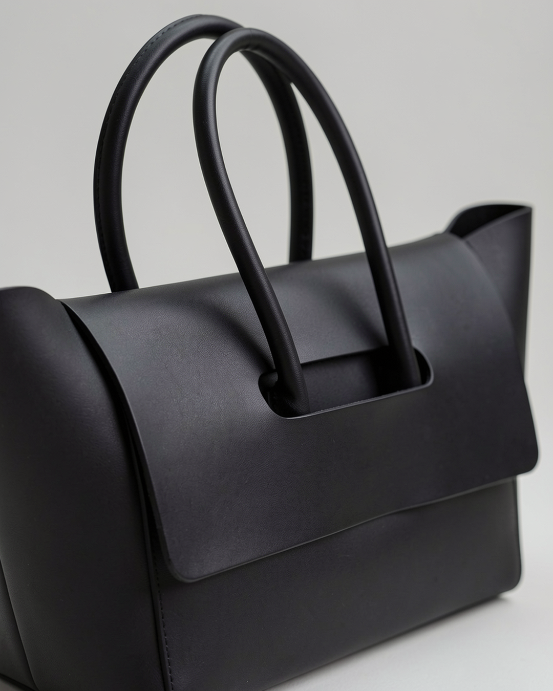 Close-up of the black structured flap tote's front flap and tubular handles