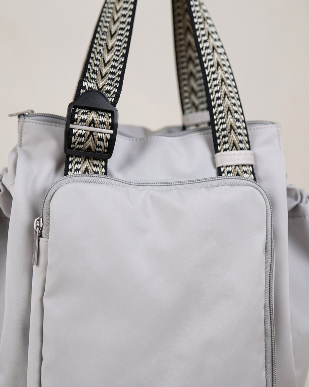Close-up of the gray drawstring pocket tote's front pocket and chevron straps