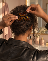 Tortoiseshell butterfly hair claw clipping curly hair up at a bathroom mirror