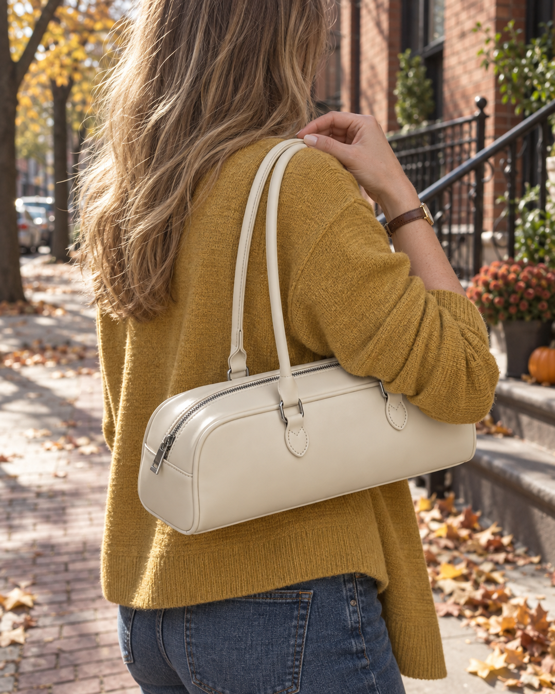 Cream baguette bag carried on the shoulder on a city sidewalk in fall