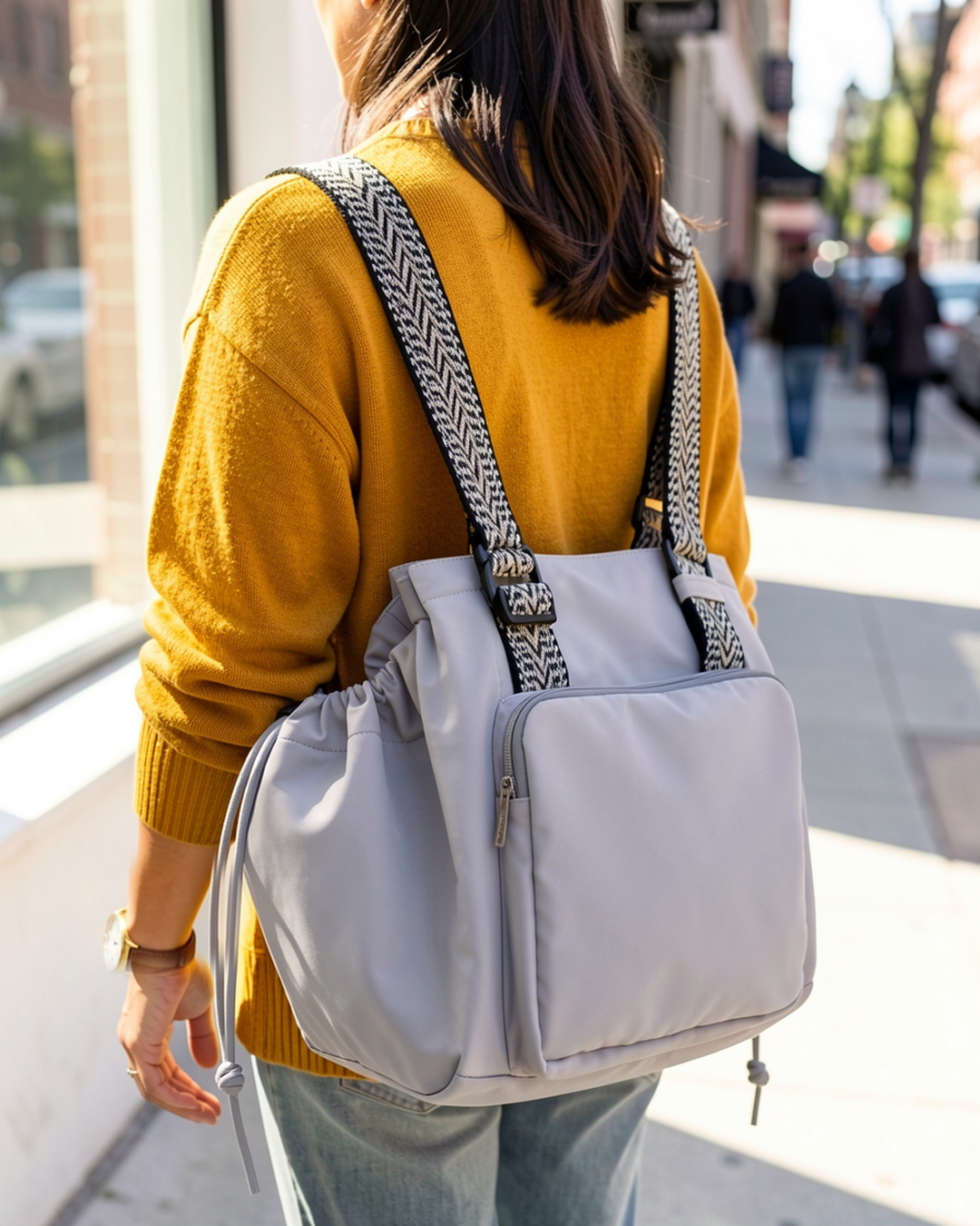 Gray drawstring pocket tote worn as a backpack on a city sidewalk
