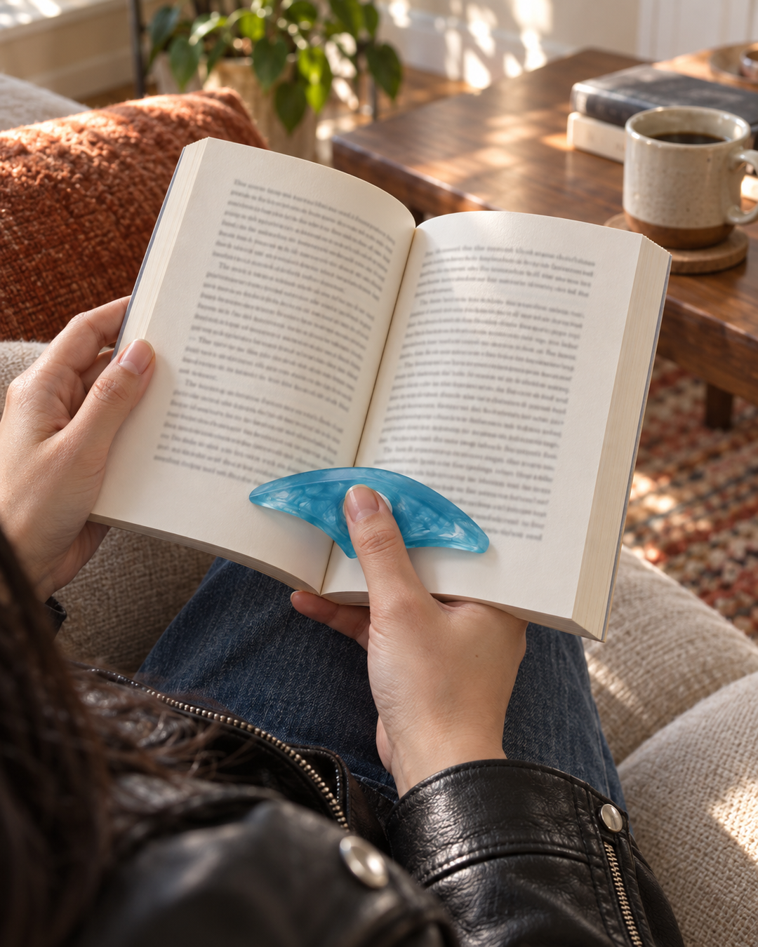 Blue resin thumb page holder holding a paperback open on the sofa