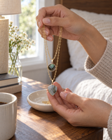 Layered stone pendant necklace lifted from a ceramic dish on a nightstand
