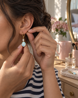 Opal-look teardrop earrings being put on at a bedroom vanity