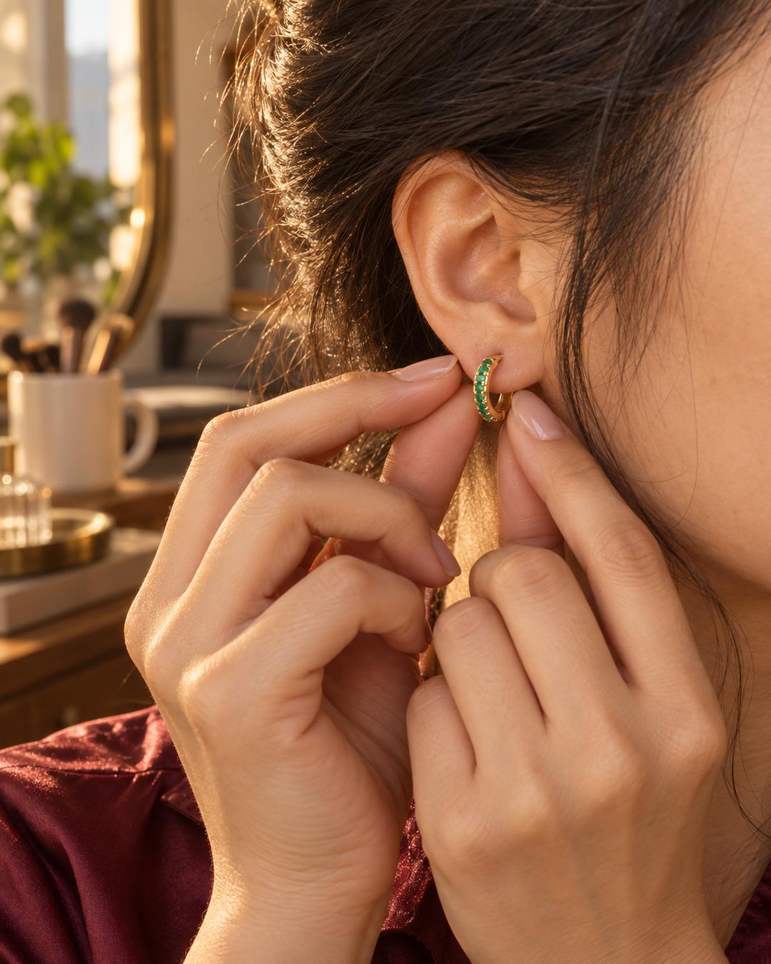Gold-tone green stone mini hoop earrings being snapped closed on the ear