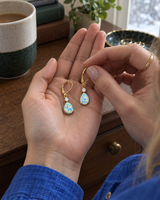 Opal-look teardrop earrings held in an open palm