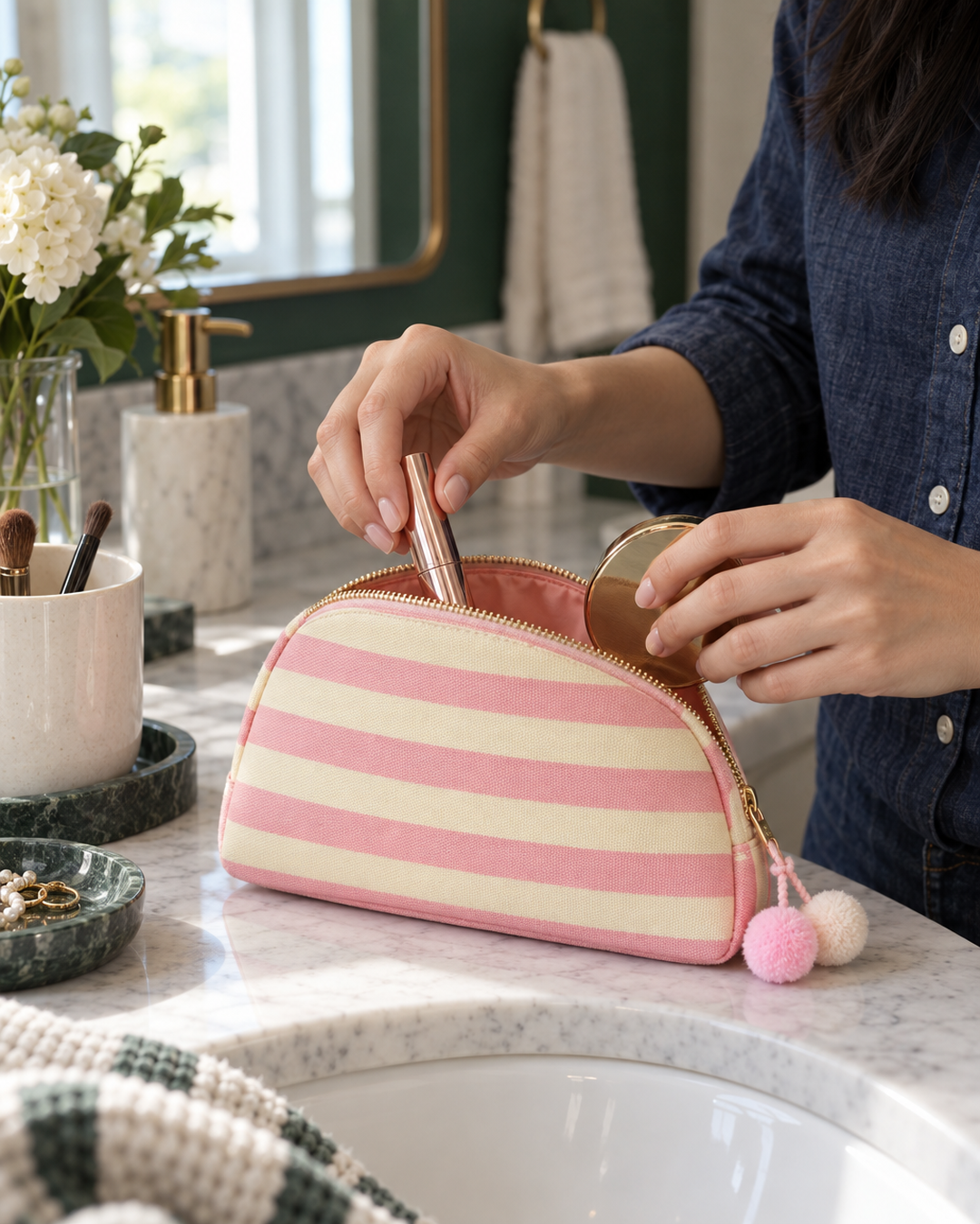 Pink striped canvas pouch being packed with makeup at a bathroom vanity
