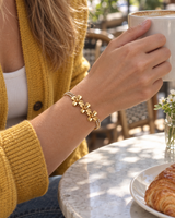 Gold-tone flower bracelet worn while lifting a cup at a cafe