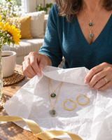 Layered stone pendant necklace and embossed gold-tone hoops unwrapped from tissue paper on a coffee table