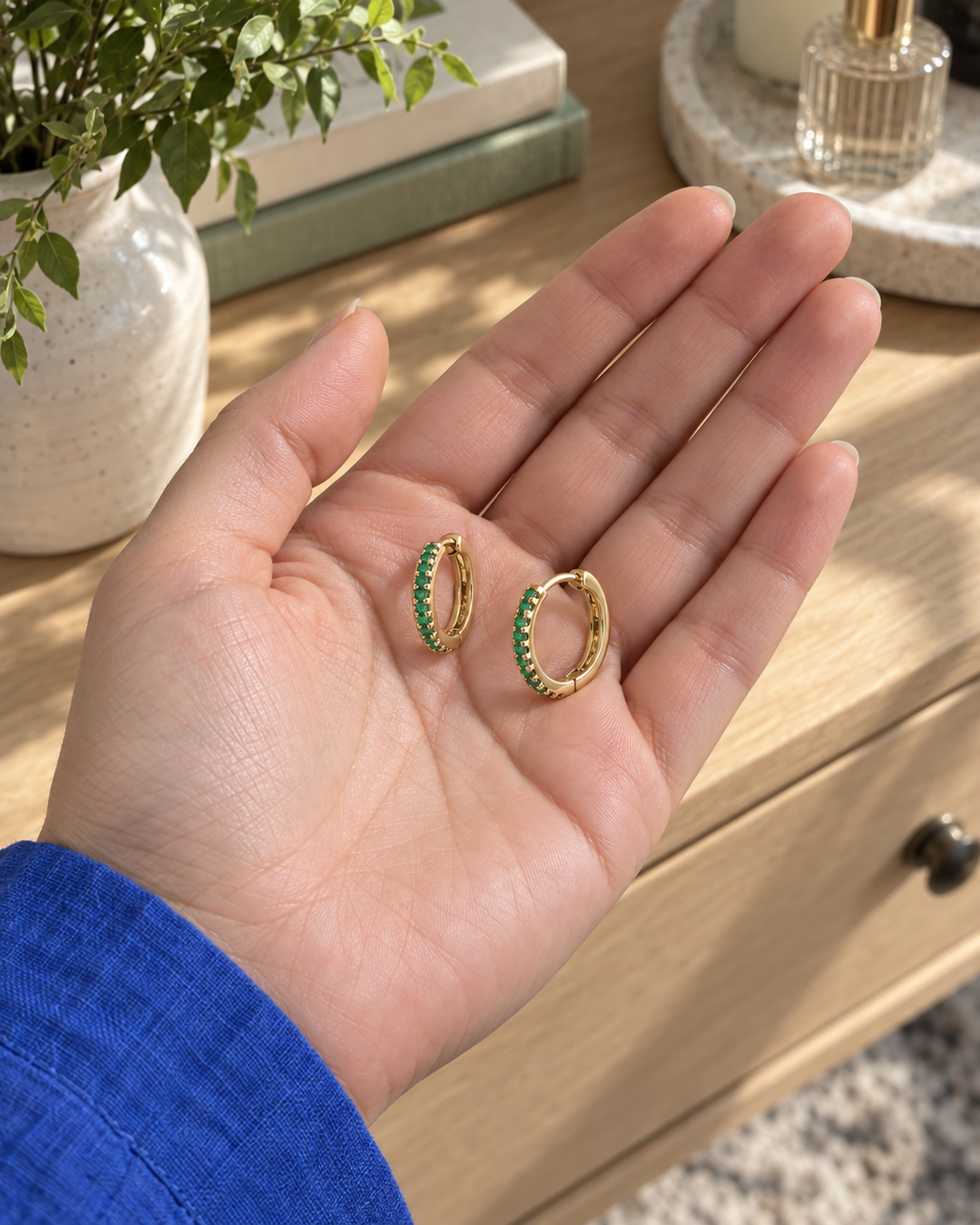 Gold-tone green stone mini hoop earrings held in a palm
