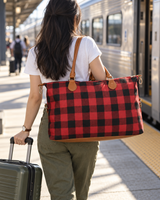 Red buffalo check weekender bag carried on a train platform with a suitcase