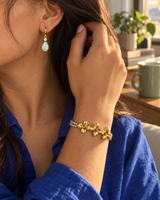 Gold-tone flower bracelet and opal-look teardrop earrings worn together, close-up of the ear and wrist