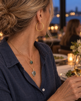 Layered stone pendant necklace and embossed gold-tone hoops worn at a restaurant dinner, rear view
