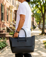 Black structured flap tote carried by hand on a city sidewalk