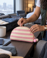 Pink striped canvas pouch zipped closed next to a suitcase in a hotel room